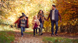 A family of four bundled up and walking through an autumnal, leafy woodland